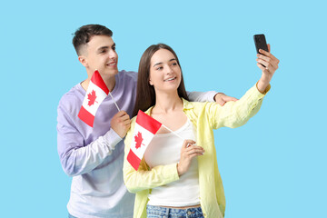 Canvas Print - Young couple with flags of Canada taking selfie on blue background