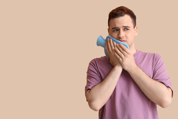 Poster - Young man with hot water bottle suffering from toothache on beige background