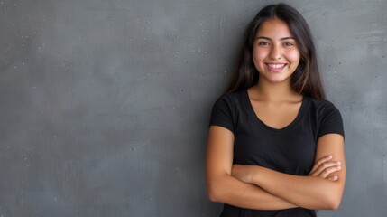 Wall Mural - A young Hispanic woman with long, dark hair stands against a grey wall, smiling cheerfully with her arms crossed. Generative AI