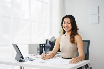 Wall Mural - Confident Asian Business Woman Working at Desk in Modern Office with Tablet and Documents