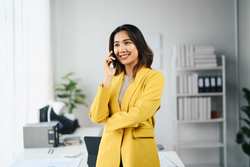 Wall Mural - Confident Asian Business Woman in Yellow Blazer Talking on Phone in Modern Office Setting