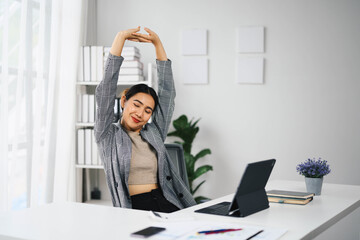 Wall Mural - Relaxed Asian Business Woman Stretching at Desk in Modern Office Environment with Laptop and Documents