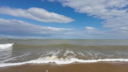 white waves crash on the beach with blue sky in the background and a white surfboarder coming ashore