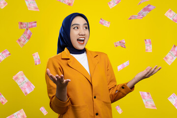 Wall Mural - Excited young Asian woman enjoying rain of money isolated on yellow background