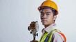 © Nany - An isolated shot of a young Asian man in a hardhat and safety vest, holding a surveyor level,