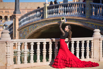 Young, beautiful, brunette woman in black shirt and red skirt, dancing flamenco in the Spain square in Seville next to a stone railing. Flamenco concept, dance, art, typical Spanish.