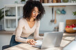 © nenetus - Cheerful attractive woman working with laptop in the kitchen at home.