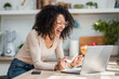© nenetus - Confident woman doing video call with laptop in the kitchen at home.