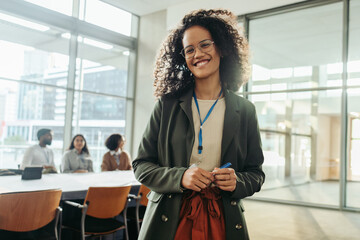 Confident young female entrepreneur smiling in modern office with colleagues in the background