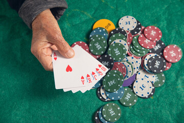 elderly female hand holding casino games chips and cards.