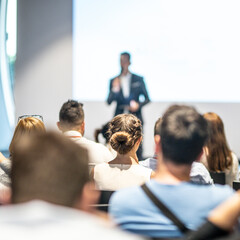 Wall Mural - Male speaker giving a talk in conference hall at business event. Audience at the conference hall. Business and Entrepreneurship concept. Focus on unrecognizable people in audience.