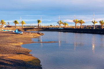 Wall Mural - Low tide in Arrecife, coastal town in Lanzarote, Canary Islands. Beach with a body of water and a few boats. The water is calm and the sky is cloudy