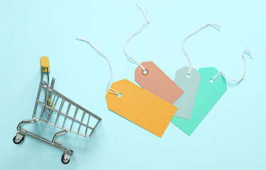 Wall Mural - Mini shopping trolley with many empty price tags on a blue background. Sale, shopping concept. Top view