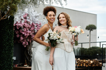 Wall Mural - Two brides in white dresses smile happily at their wedding ceremony on a rooftop.