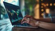© Plaifah - A pair of hands typing on a laptop, with a detailed financial graph displayed on the screen.