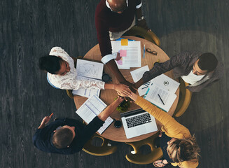 Canvas Print - Above, boardroom and people with pile of hands in meeting for teamwork, collaboration and brainstorming. Business, employees and strategy with laptop or paperwork and unity with statistics or report