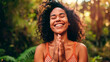 © BetterPhoto - A joyful woman with curly hair smiling with hands in prayer position in a lush green forest, expressing happiness, gratitude, and spiritual connection