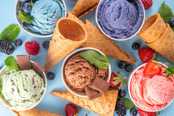 Wall Mural - Colorful bright ice cream on bowls, with waffle cones and berries, on light blue background. Variety of ice cream with different flavor with fresh berries top view copy space layout background