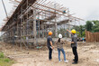 © skarie - Team of construction workers discussing project details with blueprint in construction site.