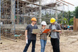 © skarie - Team of construction workers discussing project details with blueprint in construction site.