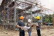 © skarie - Team of construction workers discussing project details with blueprint in construction site.
