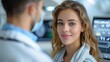 © Lens Legacy - A young woman is smiling and looking at the camera in a medical or clinical environment, with a blurred male doctor in the background, amid medical equipment.