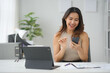 © amnaj - Smiling woman using smartphone at office desk with tablet, notebook, plant, and documents, showcasing a modern workspace and technology usage.