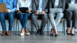 © Technical786 - Group of people sitting in row in the office, waiting for a business meeting or job interview, working on laptop notebook PCs, holding clipboards. Cropped shot, human legs, banner background