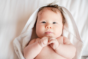 Portrait of a sweet little newborn baby girl after a bath in a white hooded towel. Baby care concept. 