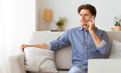 Poster - A man sits on a couch, talking on his cell phone while looking away. He is wearing a blue shirt and has a laptop in front of him.