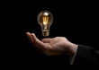 © Viktoriia - Male hand holding light bulb with black background, close up from front. Generative AI