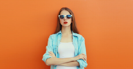 Wall Mural - Portrait of modern stylish young woman in white glasses, casual clothing posing on orange background