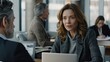 © lililia - A businesswoman sits at a desk in a modern office, using a laptop while participating in a meeting with her colleagues