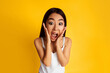 © Prostock-studio - Asian young woman with long black hair wearing a white tank top and expressing surprise. Her hands are covering her cheeks, and she has a wide, open mouth.
