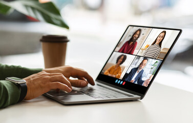 Poster - Guy sitting at a table with a laptop, using his hands to type on the keyboard. The laptop screen is displaying a video conference meeting with four participants, cafe interior