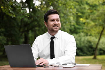 Canvas Print - Smiling businessman working with laptop at table outdoors. Remote job