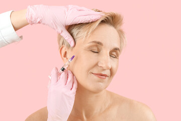 Canvas Print - Mature woman receiving filler injection on pink background, closeup