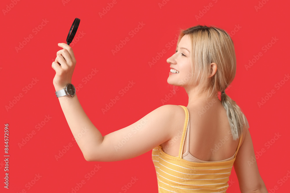 Young woman with magnifier on red background