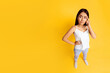 © Prostock-studio - Asian young woman standing in front of a yellow background. She is wearing a white tank top and blue jeans. She is looking to the side with a thoughtful expression on her face, top view, copy space