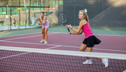 Wall Mural - Young beautiful girl in pink t-shirt and her female partner playing tennis on court