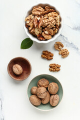 Bowls of tasty walnuts on white marble background