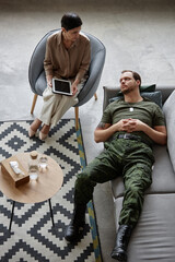 Vertical top view portrait of adult army veteran lying on couch in therapists office during consultation on mental health issues