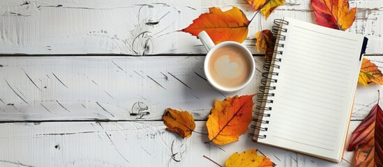 Poster - Autumn leaves and a coffee cup on a white grunge backdrop in a blank notebook with copy space image.