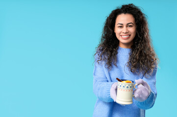 Sticker - Beautiful young African-American woman in gloves with cup of hot mulled wine on blue background