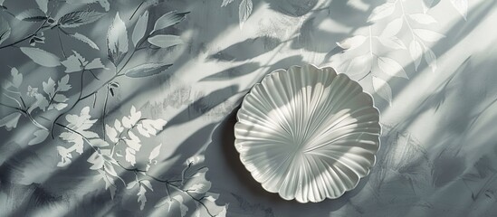 Poster - Minimalist grey interior background featuring a botanical-themed wallpaper with sunlight and shadows creating a serene atmosphere, decorative leaf-shaped plate included for a copy space image.