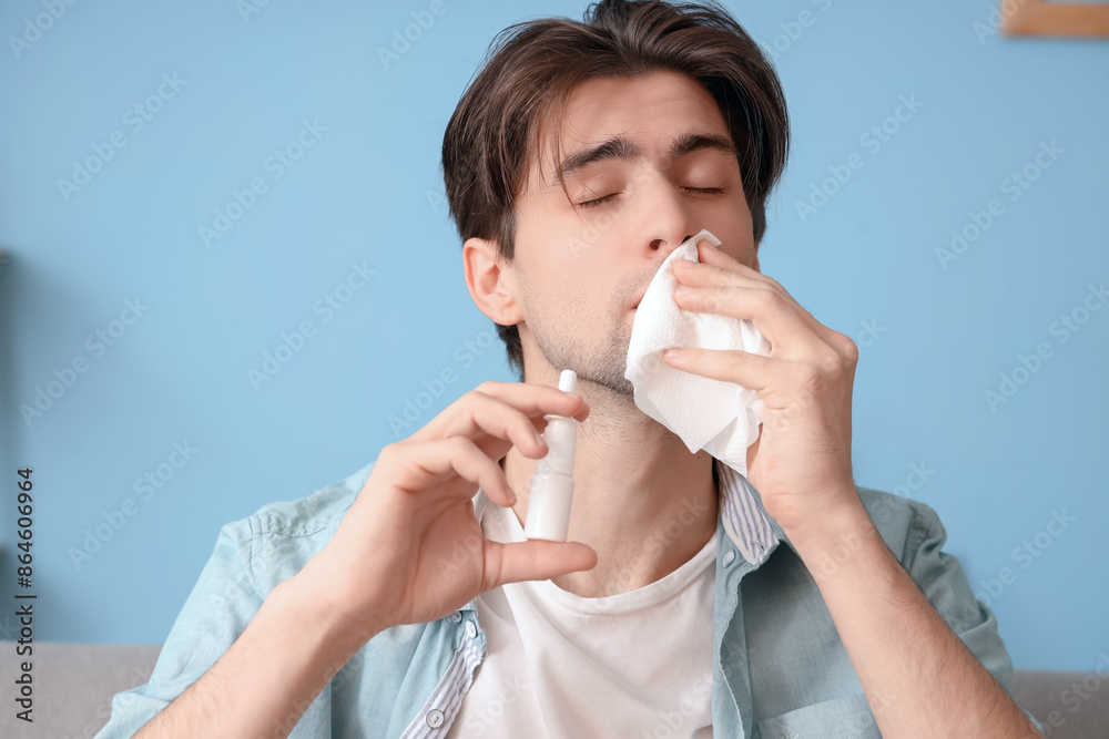 Sick young man with nasal drops and tissue sneezing at home, closeup