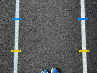 Wall Mural - Track and Field Running Lanes. Overhead view of a rubber black running track surface with white lane lines. Yellow and blue dashed lines at the center of view. A running stands at the edge of view. 