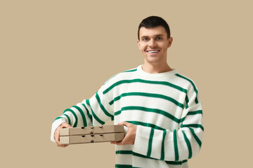 Young man holding cardboard boxes with tasty pizzas on beige background