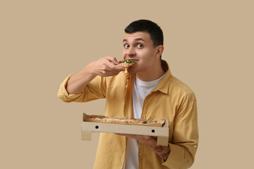 Poster - Young man eating piece of tasty pizza and holding cardboard box on beige background