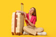 © Pixel-Shot - Beautiful young woman with suitcase sitting against yellow background